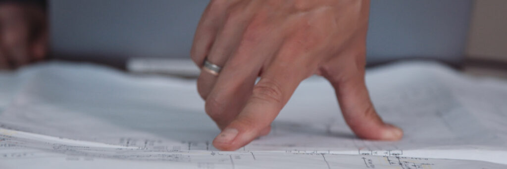 The picture shows a hand pointing to drawing of a plant documentation from Menger Group.